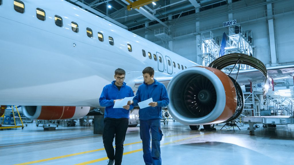 Aircraft maintenance mechanic uses tablet in front of an airplane cabin in a hangar.