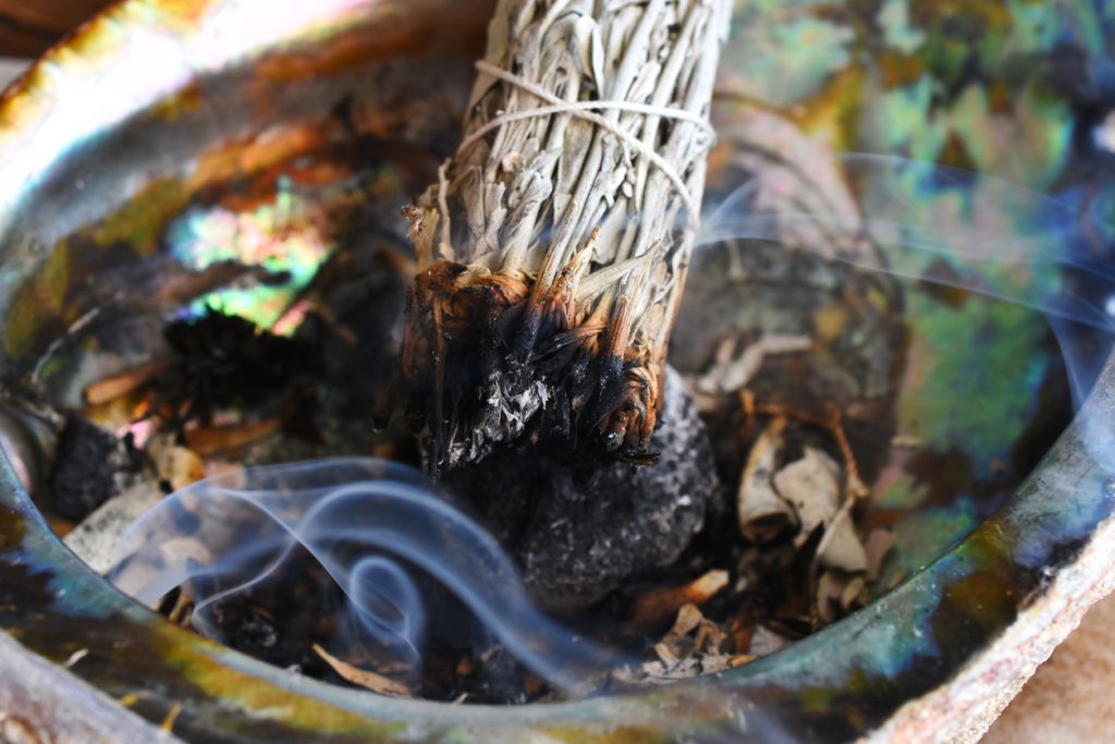 A close up image of a burning white sage bundle in an abalone shell.