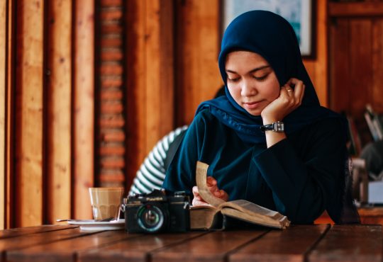 Woman wearing hijab reading book in cafe