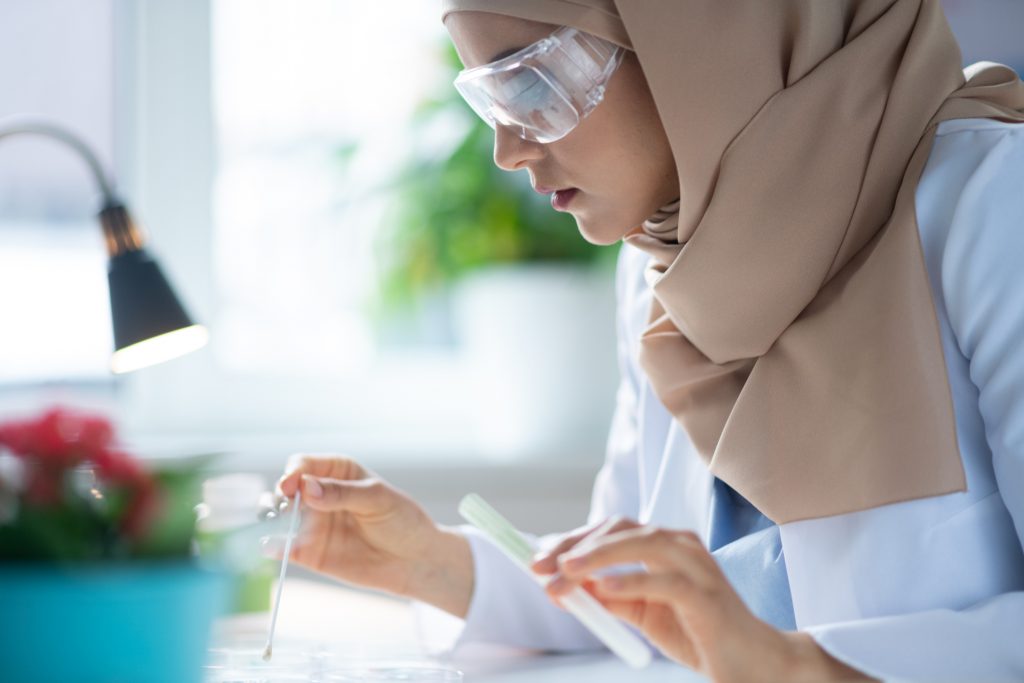 Protective glasses. Female chemist wearing protective glasses and hijab making some experiment