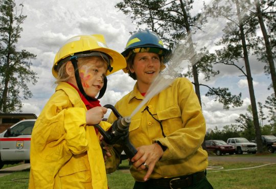 child with firefighter holding hose and spraying water