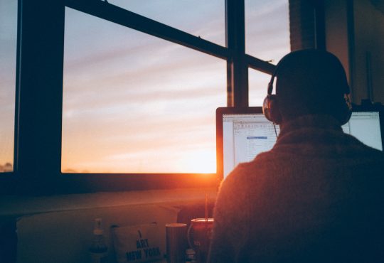 man sitting at desk in front of computer screen with headphones on