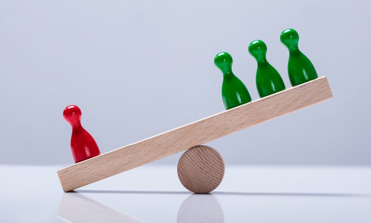 Red And Green Pawns Figures Balancing On Wooden Seesaw