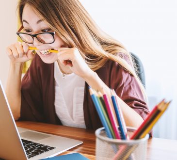 frustrated woman looking at computer and biting pencil