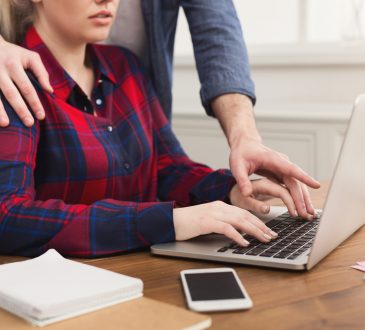 man touching shoulder and hand of woman working on laptop