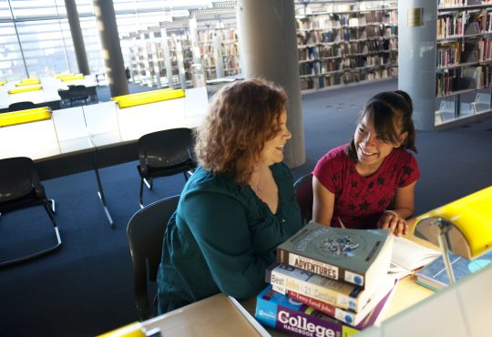 female mentor and mentee sitting together in library