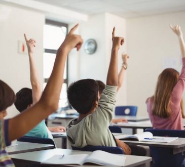 children with hands raised in classroom