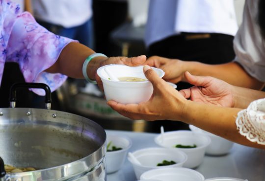 woman handing bowl of soup out in kitchen