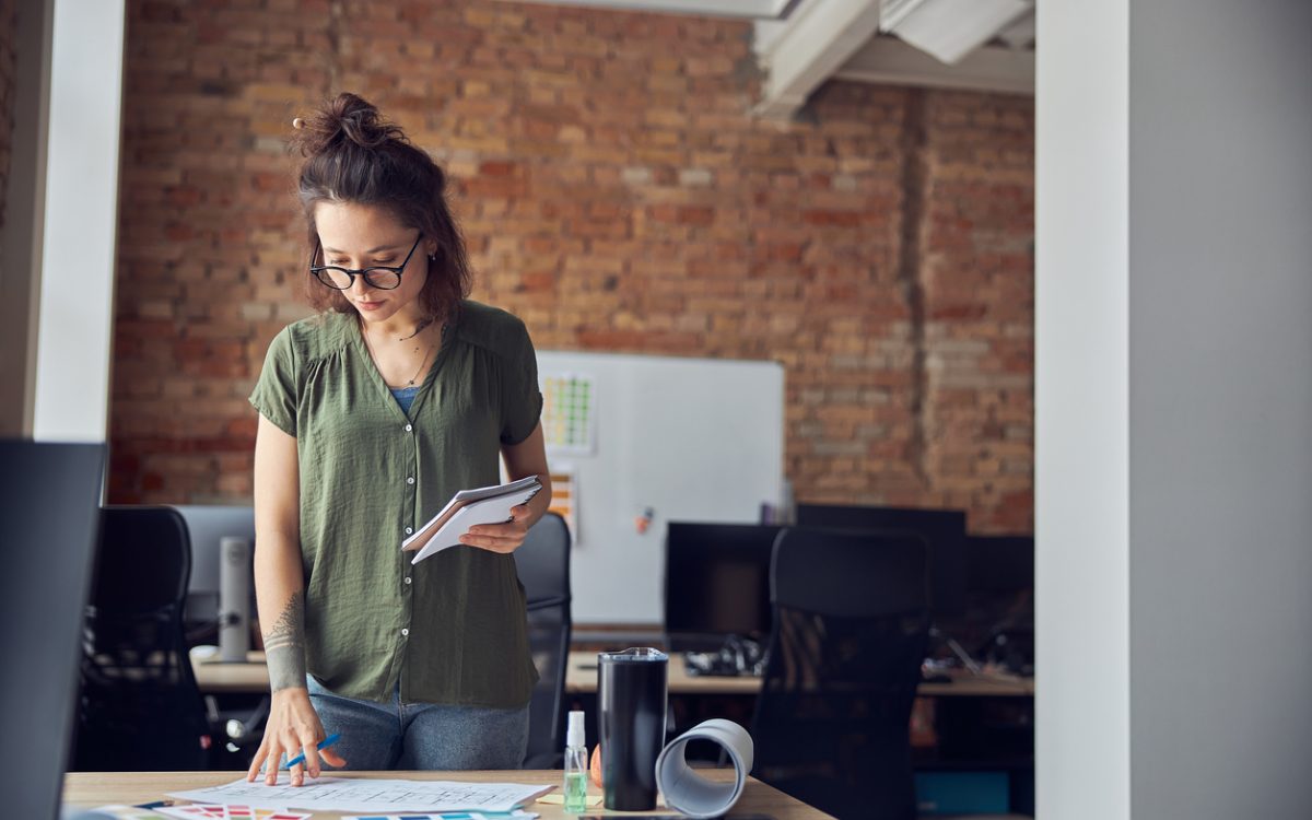 Interior designer or architect in casual wear with messy hairdo making notes while looking at a blueprint
