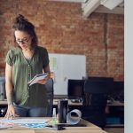 Interior designer or architect in casual wear with messy hairdo making notes while looking at a blueprint