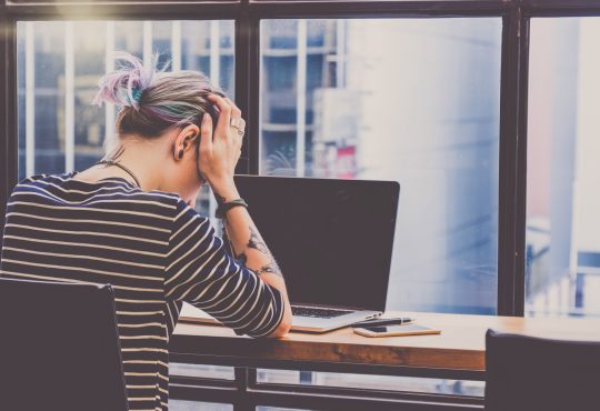 person with head in hands in front of computer