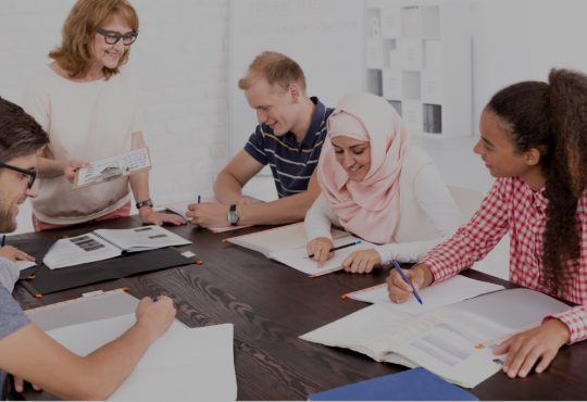 diverse group of people sitting around table listening to instructor