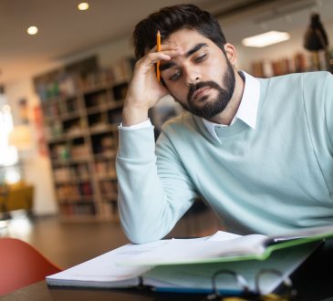 Exhausted young man student studying in a college library