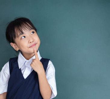 little Girl thinking with finger on chin against green blackboard