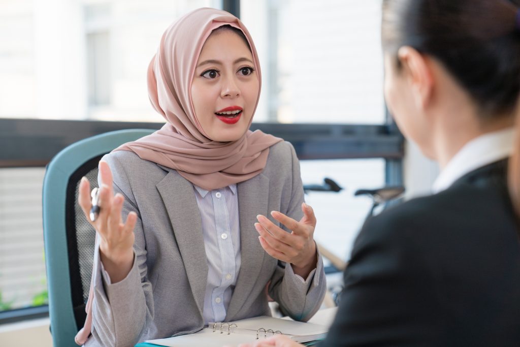 woman wearing hijab talking to other woman in office