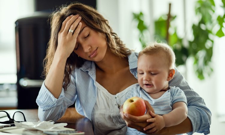 Young mother feeling exhausted while being with her baby and working at home.