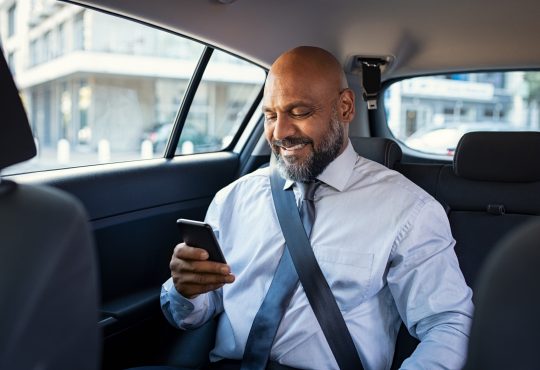 man reading on phone in back of car