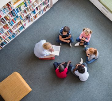 Teacher reading fairy tales to children sitting in a circle at library.