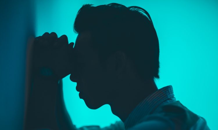 man leaning head on hands against wall