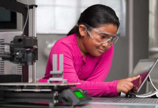 A young student wearing pink is working on a touchscreen making changes to a 3d printed toy in a summer school tech class.