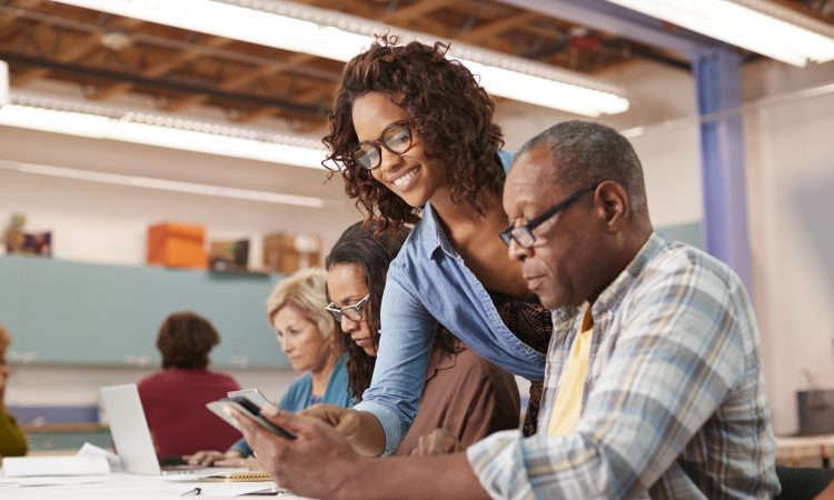 Teacher Helping Retired Senior Man Attending IT Class In Community Centre
