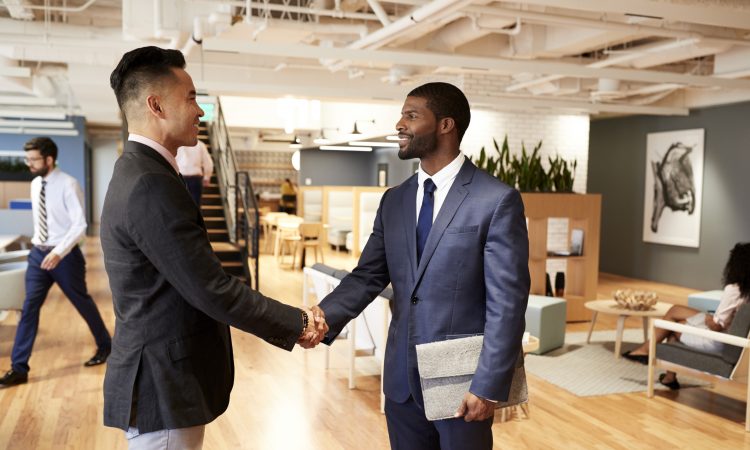 Two Businessmen Meeting And Shaking Hands In Modern Open Plan Office