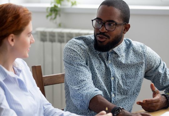 man and woman sitting and talking in office