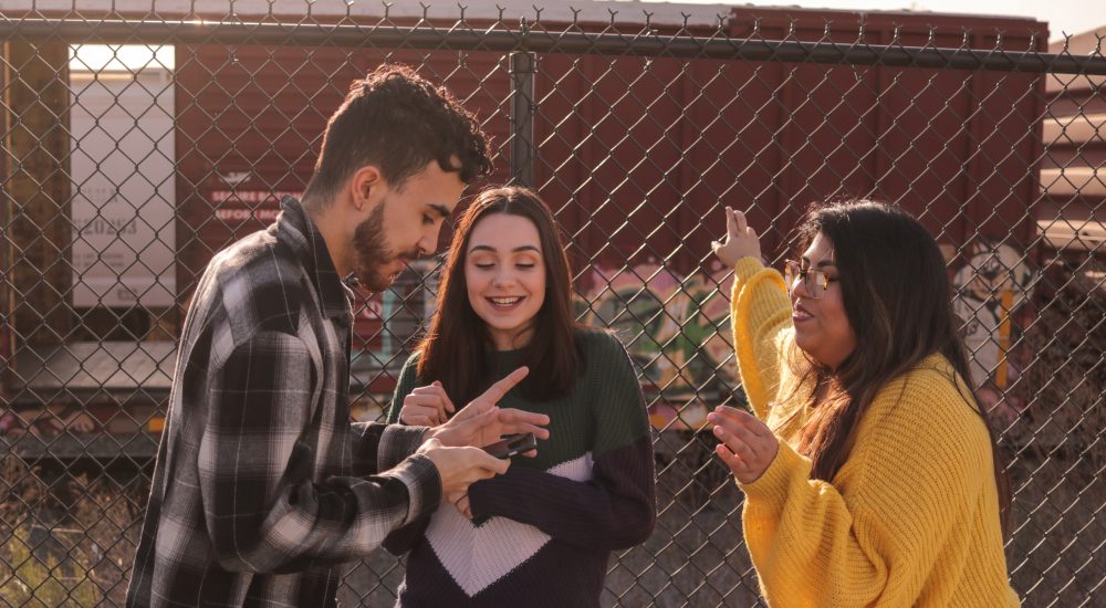 three young people talking by chain link fence