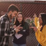 three young people talking by chain link fence