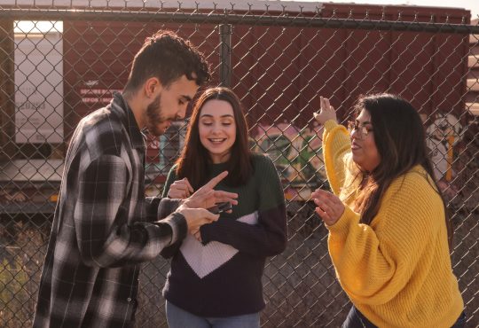 three young people talking by chain link fence