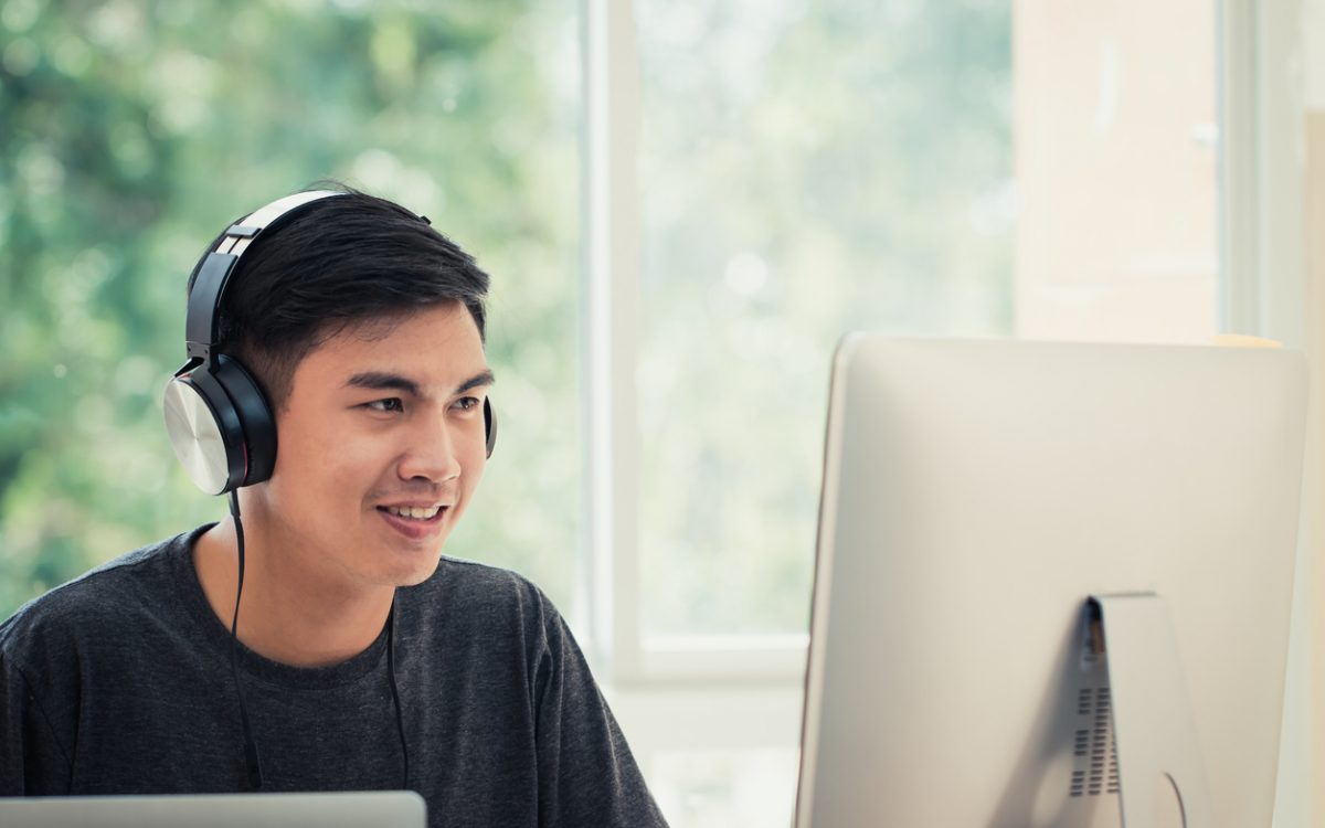 Male student on computer at home wearing headphones