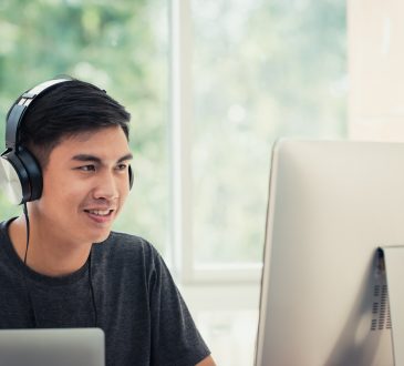 Male student on computer at home wearing headphones