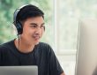 Male student on computer at home wearing headphones