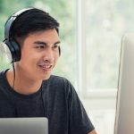 Male student on computer at home wearing headphones