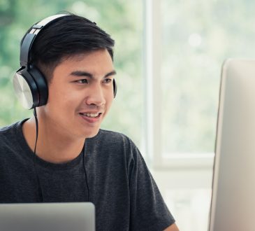 Male student on computer at home wearing headphones