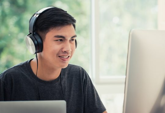 Male student on computer at home wearing headphones