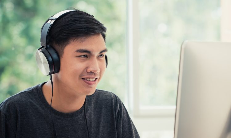 Male student on computer at home wearing headphones