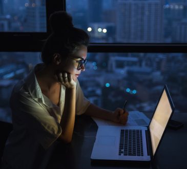 Woman is working with laptop at home during night.