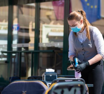 Waitress with a mask disinfects the table of an outdoor bar