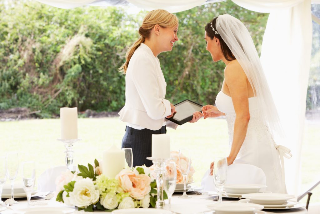 Bride With Wedding Planner In Marquee Using A Digital Tablet