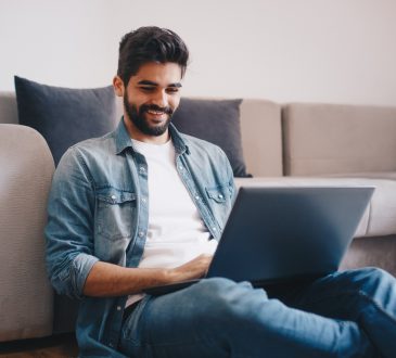 Young relaxed man working on laptop while sitting on floor at home