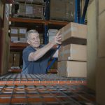 Smiling middle aged man stacking boxes in distribution warehouse
