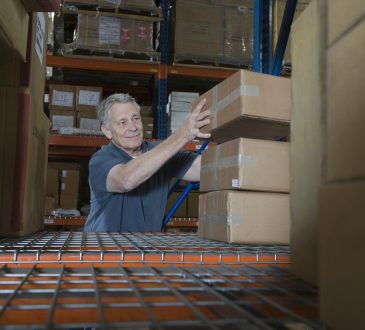 Smiling middle aged man stacking boxes in distribution warehouse