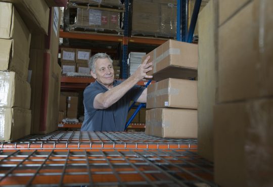 Smiling middle aged man stacking boxes in distribution warehouse