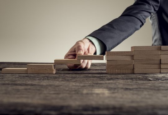 businessman forming a bridge of wooden building blocks in a gap in a set or steps
