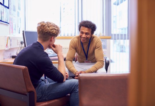 Male College Student Meeting With Campus Counselor Discussing Mental Health Issues