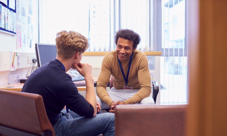 Male College Student Meeting With Campus Counselor Discussing Mental Health Issues