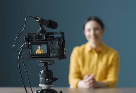 Smiling woman sitting in front of a camera and making a video blog