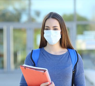 Front view of a student wearing a protective mask walking in a campus