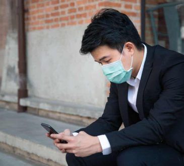 male student in suit looking at phone wearing mask